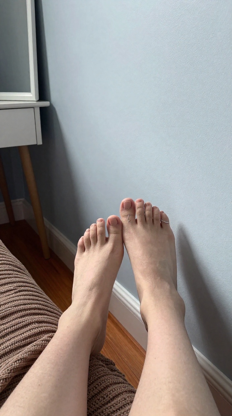 Bare feet with silver toe ring sliding down cold wall, bedroom vanity mirror, diffused daylight, copper and espresso tones, knit fabric texture.